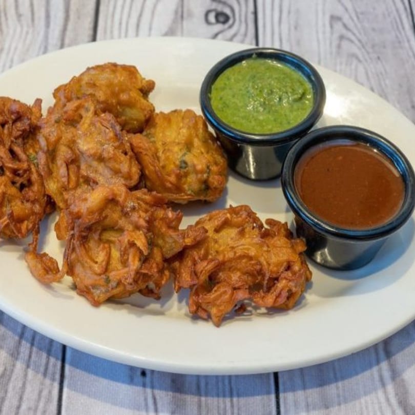 Golden-brown Indian onion pakoras on a white plate, served with green and brown dipping sauces.