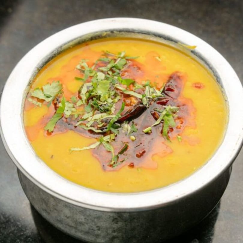 A bowl of yellow Indian dal, topped with red oil and green cilantro.