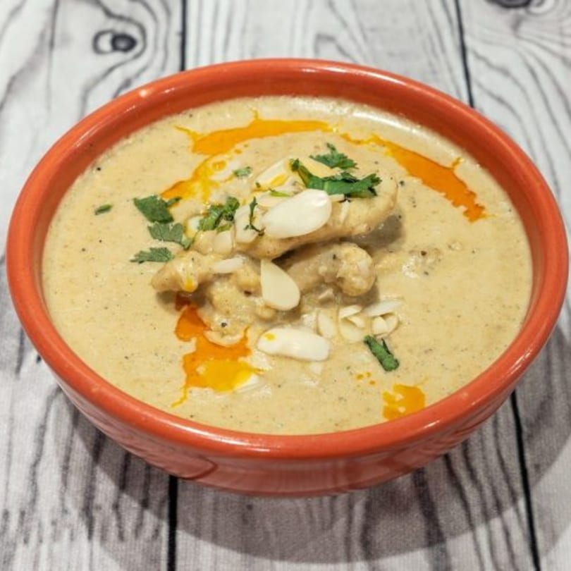 Creamy Indian chicken korma in an orange bowl, garnished with almonds and cilantro.