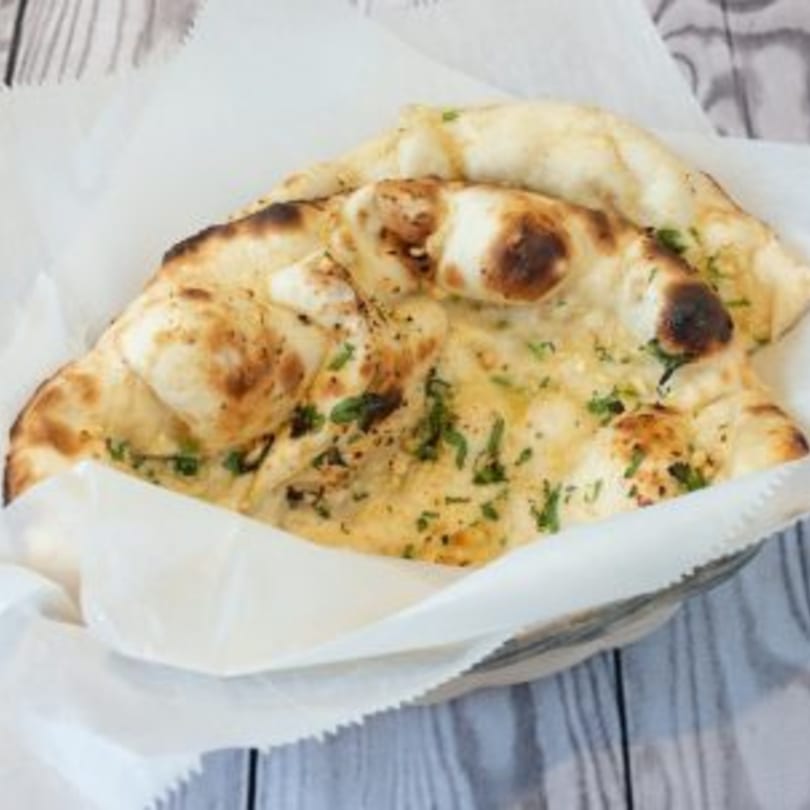 Two pieces of golden-brown Indian naan bread, garnished with green herbs, served in a white paper-lined basket.