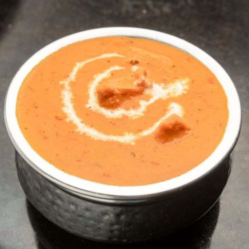 A close-up of The Kurrywala Co.'s butter chicken, a creamy orange curry with white cream swirls.