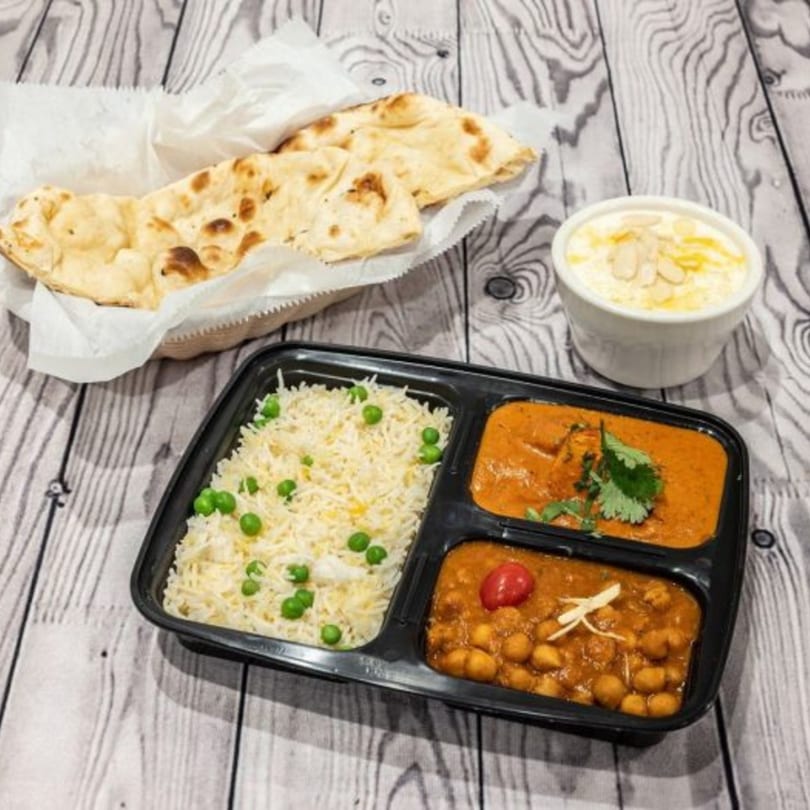 Indian meal with naan, rice, two curries, and a dessert on a wooden table.