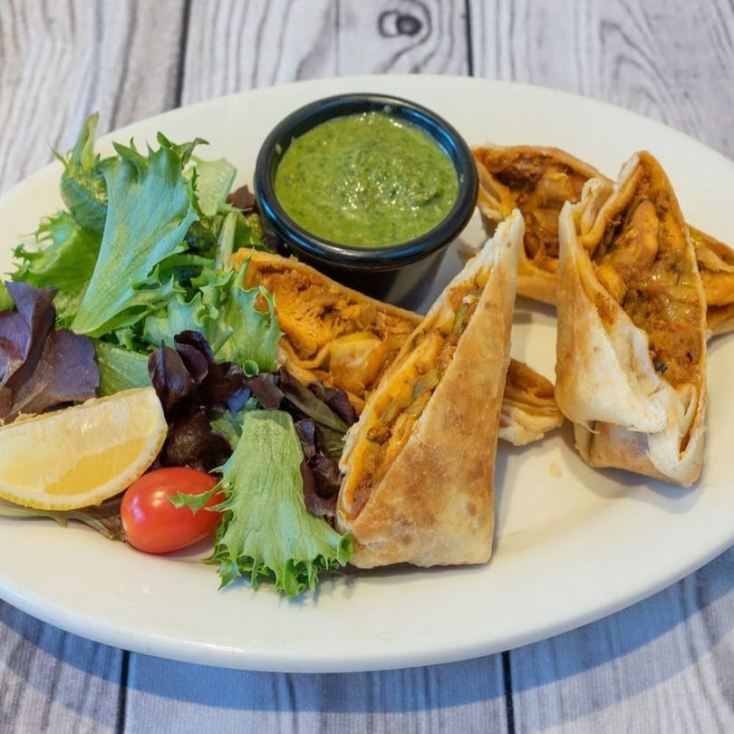 Indian samosa-like pastries with green chutney, a lemon wedge, cherry tomato, and mixed greens.
