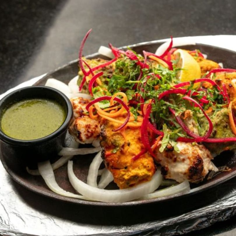 Indian chicken tikka, garnished with herbs, red peppers, and lemon, served with green chutney.