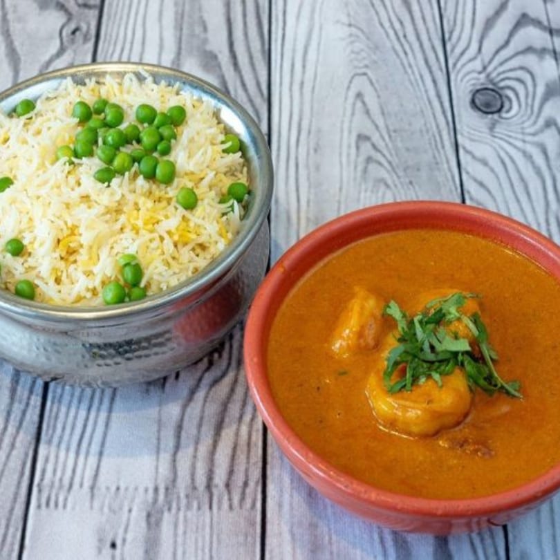 A bowl of Indian curry with shrimp and cilantro next to a bowl of rice with green peas.